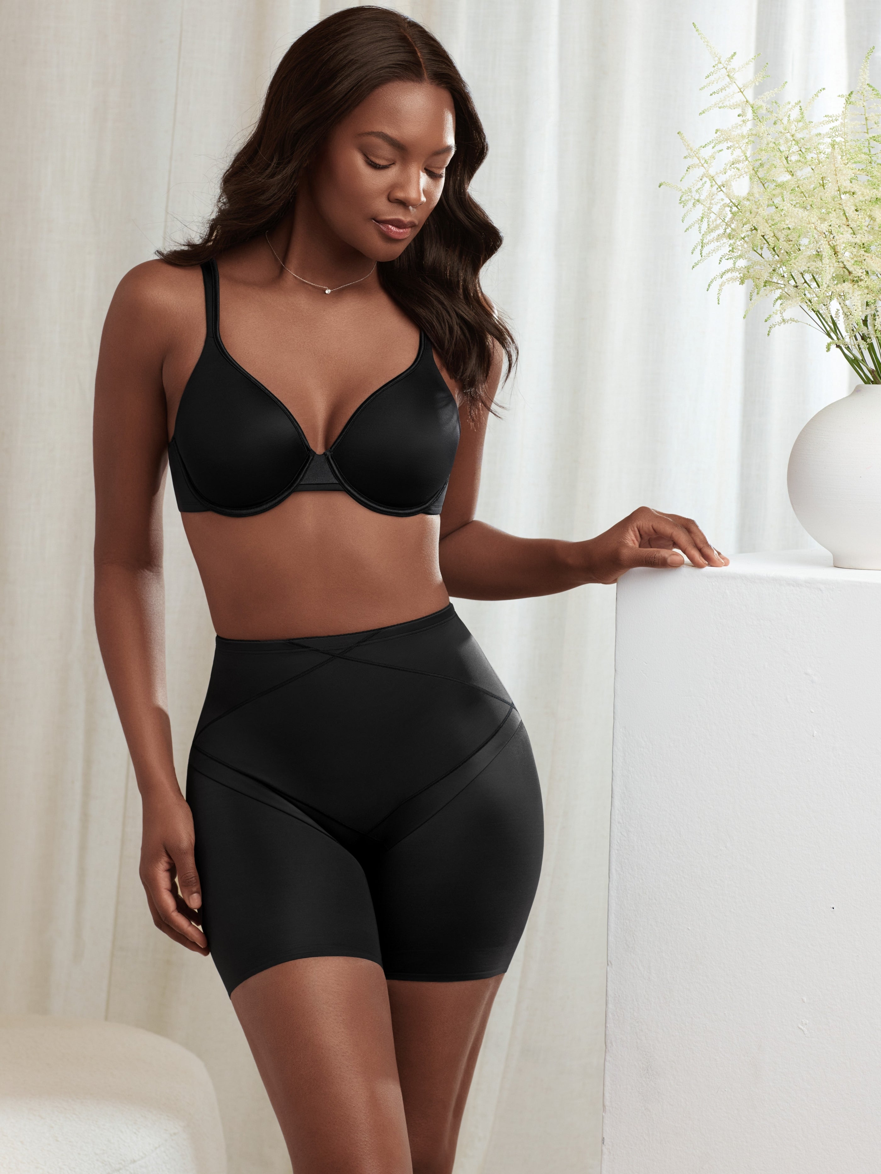 a woman standing in a bedroom wearing a black tummy control short body shaper all-groups
