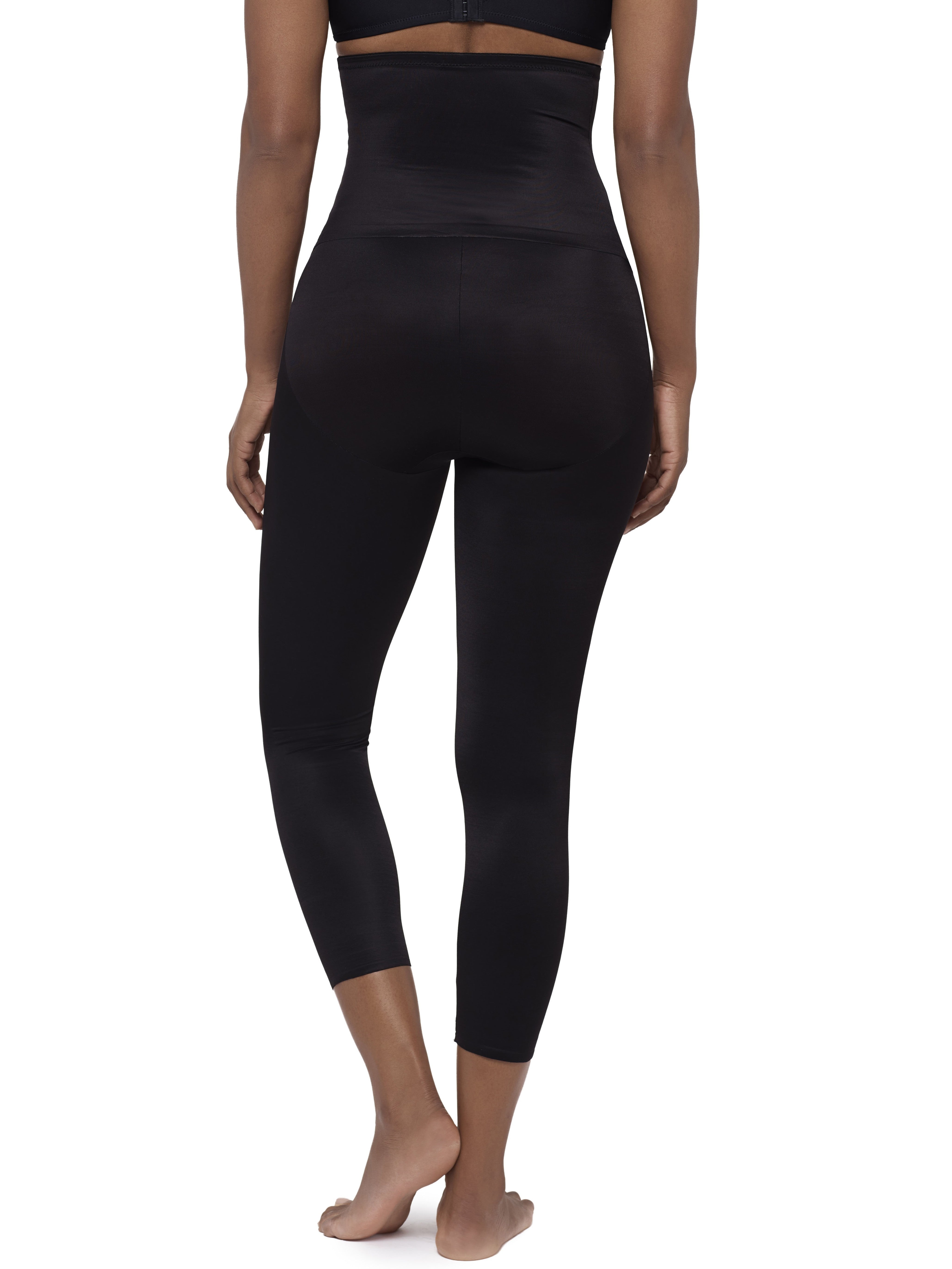 Rear view of a model wearing black high-waisted capri leggings and a matching black sports bra against a plain white background.