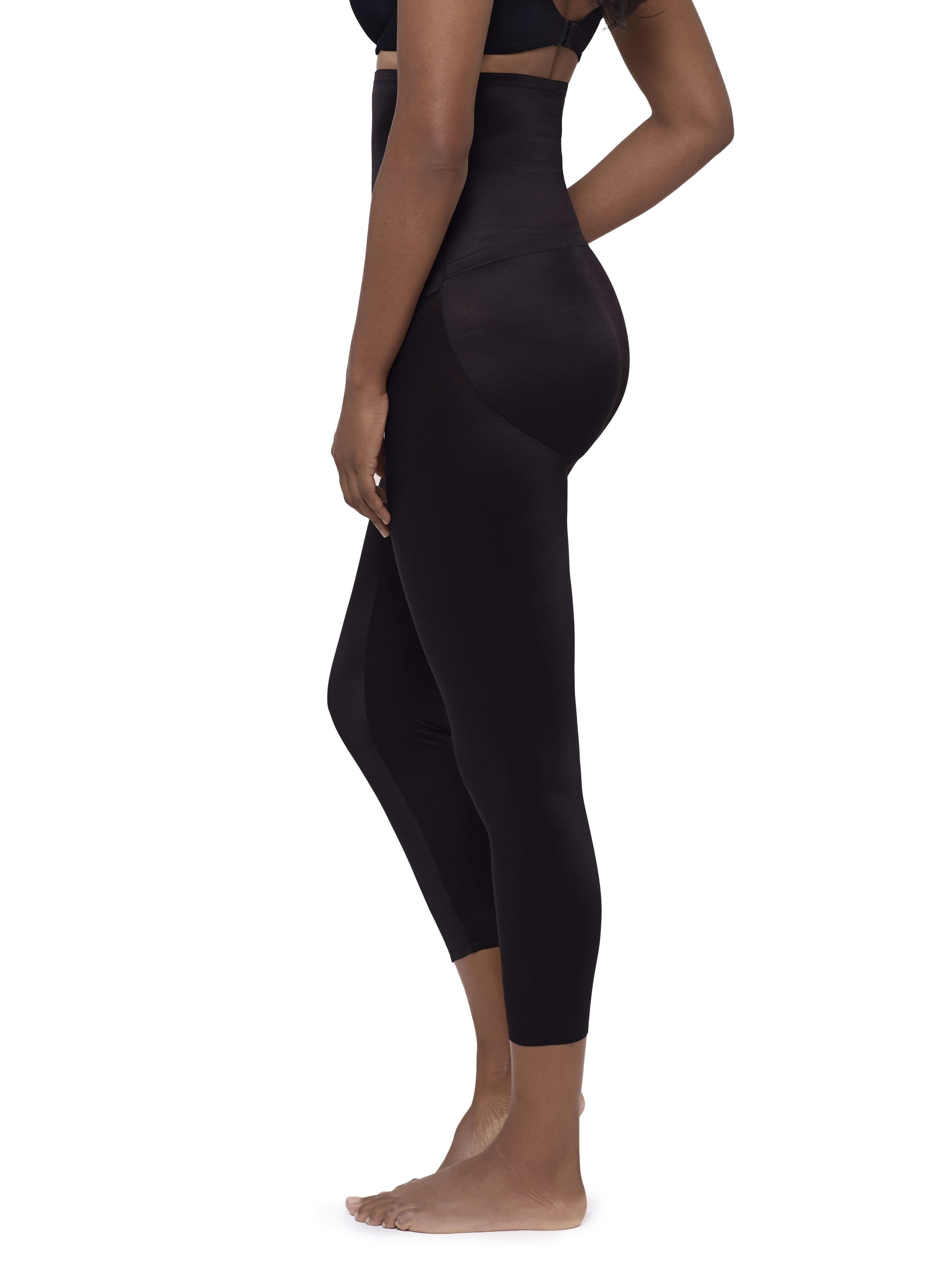 A side-profile view of a model wearing high-waisted black shapewear leggings against a plain white background.