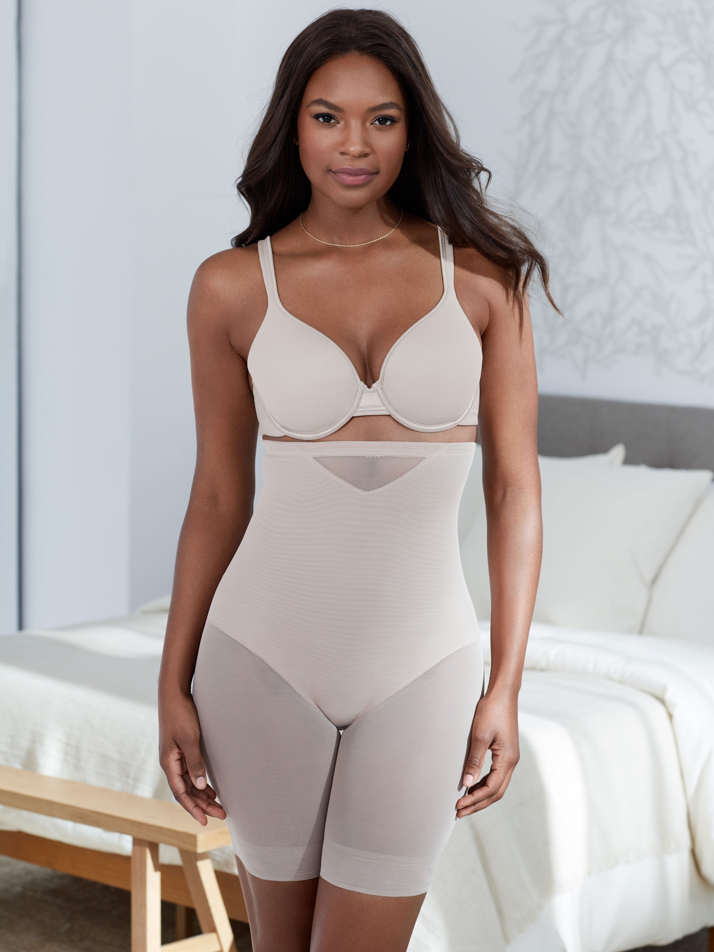 a woman standing in a bedroom wearing a nude high waisted sheer shapewear short body shaper all-groups