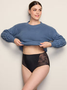 a woman lifting up her blue sweater to show herself wearing a black lace brief panty