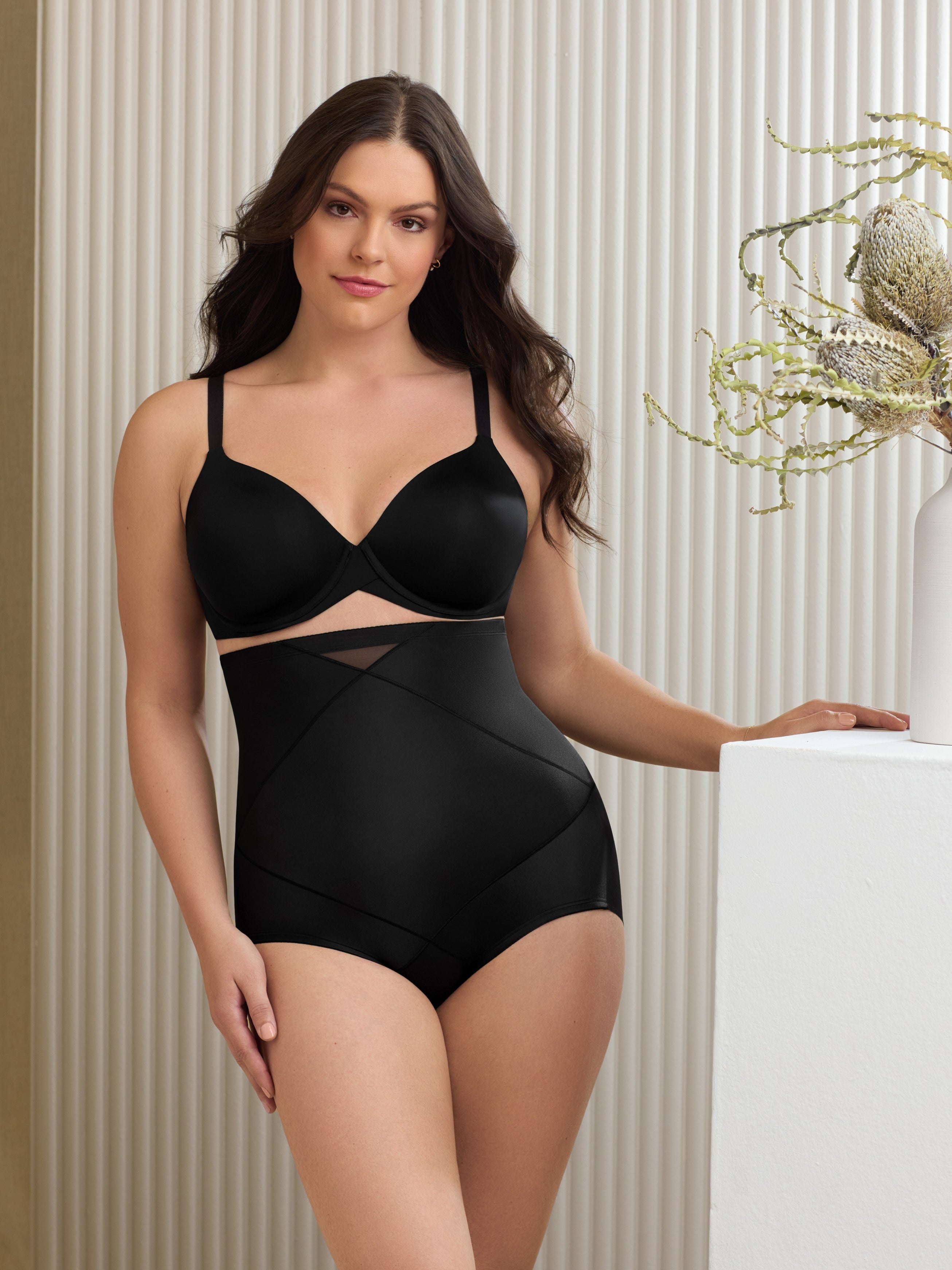 a woman in a living room wearing a black high waisted tummy control shaping brief shapewear 