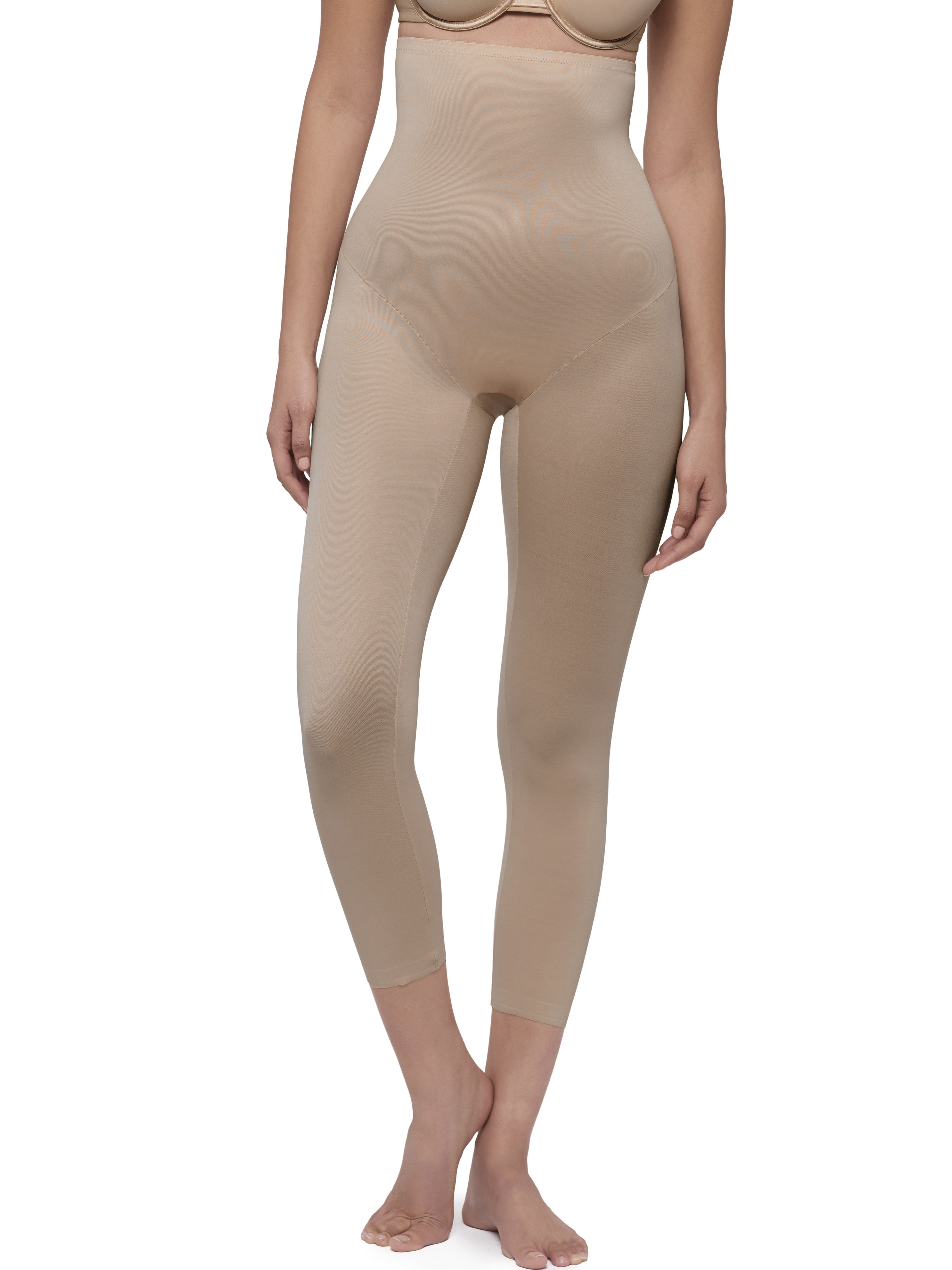 A model wearing high-waisted, full-length shapewear leggings in a nude beige color, shown from the chest down against a plain white background.