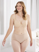 a woman standing in a living room while wearing a beige bra and a beige tummy control top brief body shaper shapewear