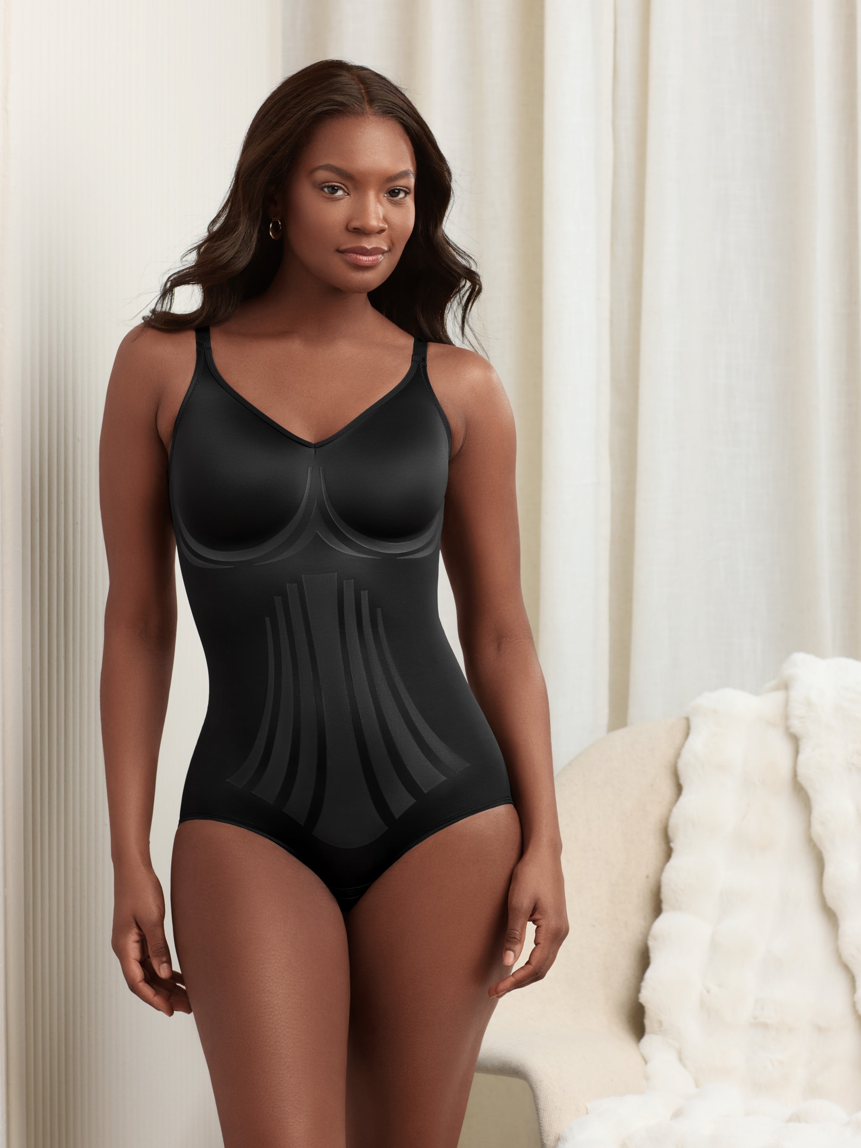 a woman standing in a bedroom wearing a black shaping bodysuit body shaper shapewear all-groups