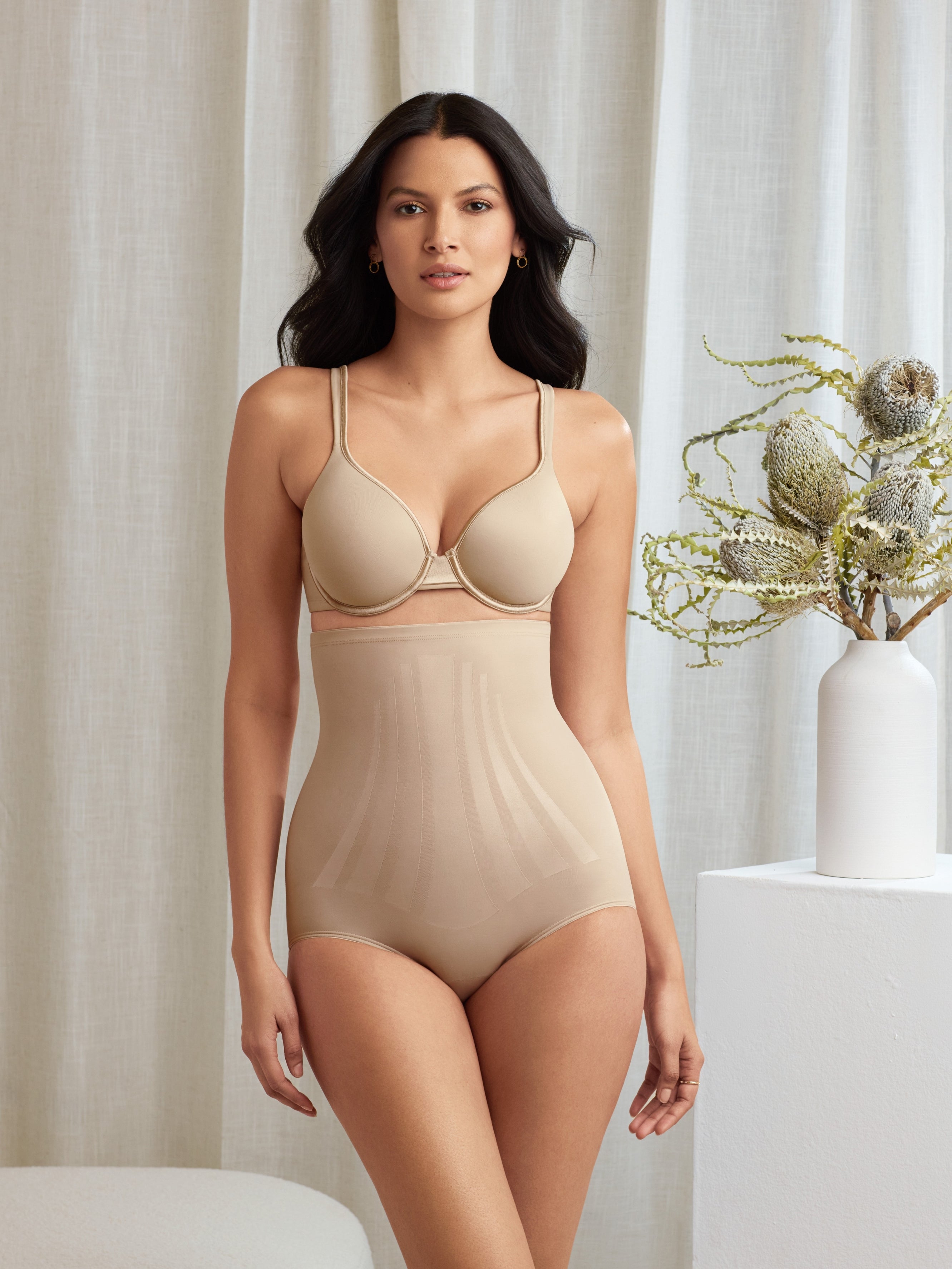 a woman standing in a bedroom wearing a nude high waisted tummy control brief shapewear