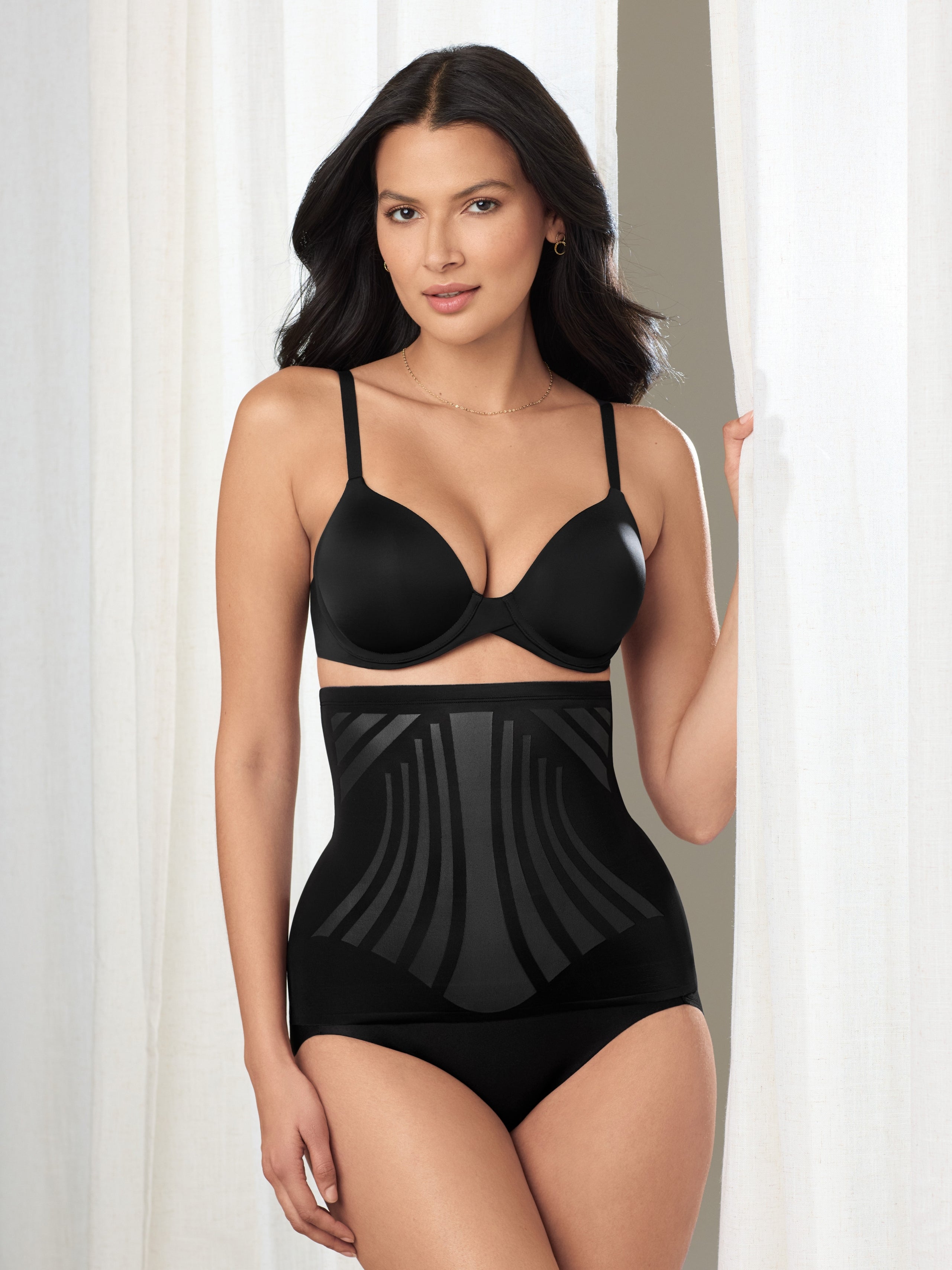 a woman standing in a curtain wearing a black waist cincher body shaper shapewear all-groups