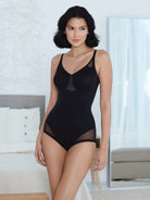 a woman standing in a bedroom a woman wearing a black sheer tummy control body shaper bodysuit shapewear