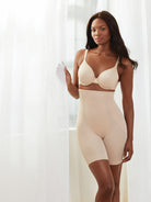 a woman standing next to a window wearing a nude high waisted tummy control shapewear short all-groups