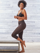 a woman wearing back tummy control leggings kneeling on a bench against a grey brick wall all-groups