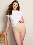 a woman wearing a white t-shirt and a nude control top panty leaning on a wooden stool all-groups