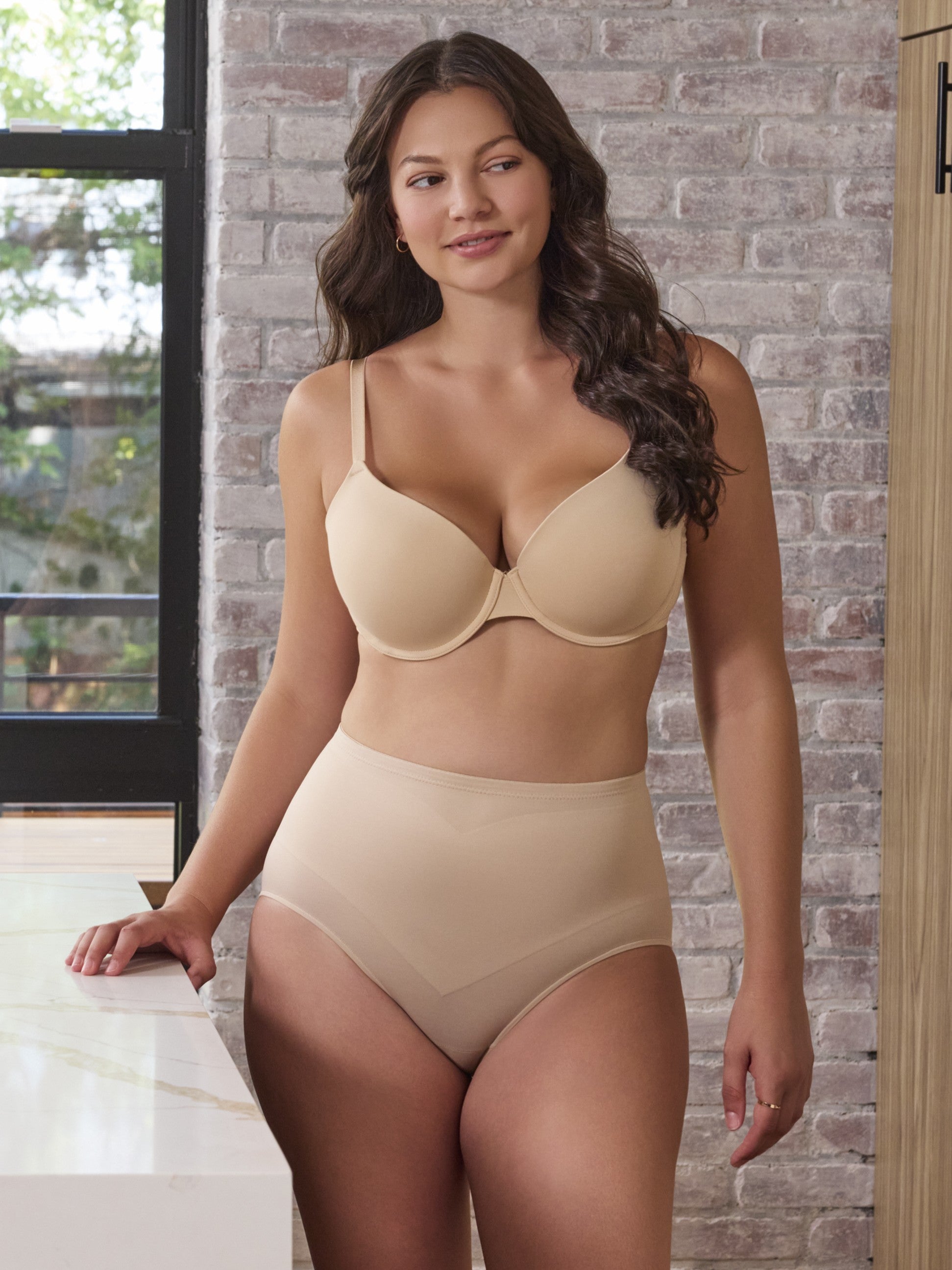 a woman standing in a kitchen wearing a beige tummy control panty shaping brief shapewear all-groups