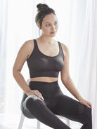 a woman sitting on a stool in front of white curtains wearing black leggings and a black shaping bralette