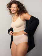 a woman wearing a black cardigan, nude shaping bralette, and a nude brief panty