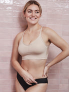 a woman standing next to a pink wall wearing a nude shaping wireless bra bralette