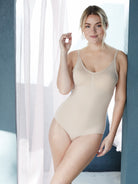 a woman leaning on a blue wall in front of a window wearing a nude body shaper shaping bodysuit shapewear all-groups